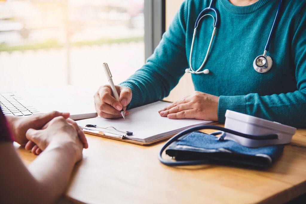 Un professionnel de santé prend des notes pendant une consultation, face à un patient
