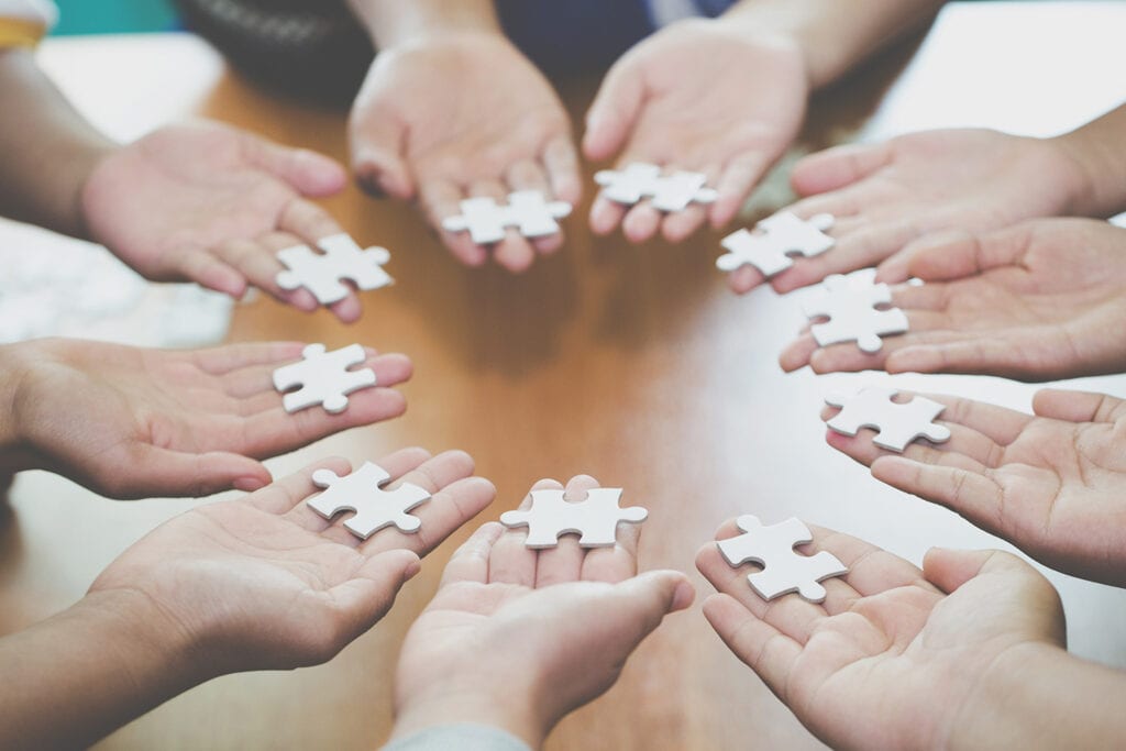 Des mains réunies en cercle, chacune tenant une pièce de puzzle